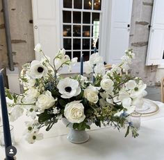 an arrangement of white flowers in a vase sitting on a table with blue candlesticks