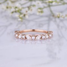 a rose gold wedding band with white pearls on the side and flowers in the background