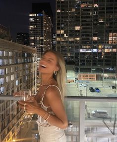 a woman standing on top of a building holding a wine glass in front of her face