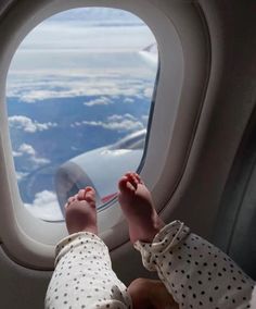 a baby looking out an airplane window at the clouds and water below it, with their feet propped up