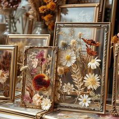 three framed pictures with flowers in them on a table next to other frames and vases