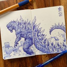 a notebook with a drawing of a godzilla on it next to a pen and marker