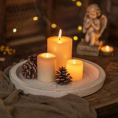 three lit candles on a plate with pine cones and angel figurines in the background