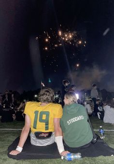 two people sitting on the ground watching fireworks