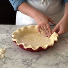 a woman is kneading dough into a pie dish