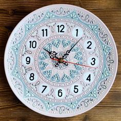 a white clock on a wooden surface with numbers and symbols around the clock is shown