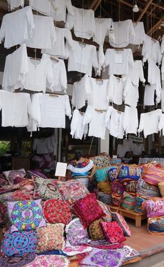 many colorful pillows and blankets are on display in a market area with hanging laundry lines