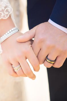 a close up of two people holding hands with rings on their fingers and wearing wedding bands