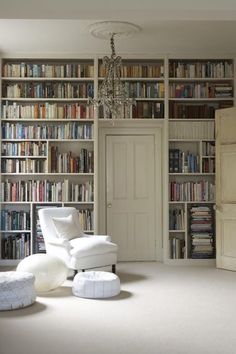 a living room filled with lots of bookshelves next to a white chair and ottoman