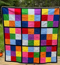 a multicolored quilt is hanging on a wooden deck in front of some trees