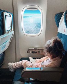 a woman sitting in an airplane seat looking out the window at the ocean and sky