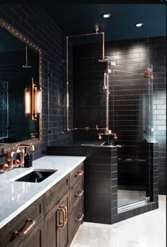 a bathroom with black tiles and copper fixtures on the walls, along with two sinks