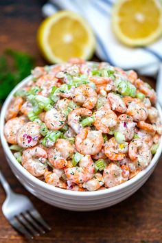 a white bowl filled with shrimp salad next to a fork and lemon wedged garnish