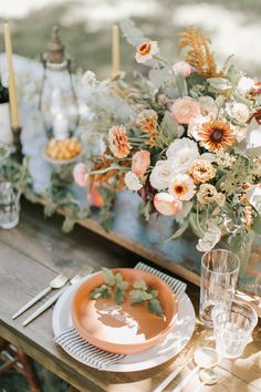 an arrangement of flowers and candles on a table with plates, glasses and napkins