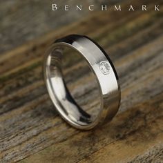 a white gold wedding ring with a diamond in the center on a wooden surface,