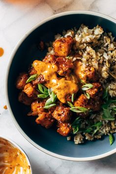 a blue bowl filled with rice and meat covered in sauce on top of a table