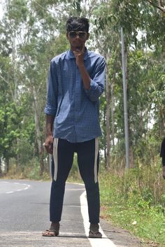 a man standing on the side of a road talking on a cell phone while holding his hand up to his mouth