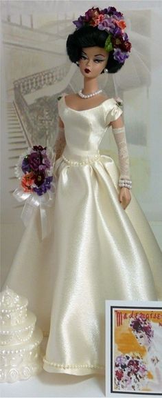 the doll is wearing a white dress with flowers in her hair and holding a bouquet