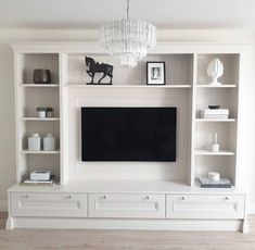 a white entertainment center with built in shelving and chandelier