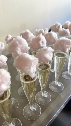 there are many champagne flutes with pink flowers in them on the table and one is filled with cotton balls