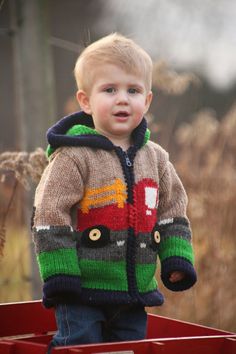 a little boy standing in the back of a red wagon with his hands in his pockets