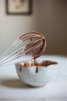 a whisk in a white bowl with chocolate sauce on the side and brown sprinkles coming out of it