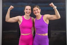 two women in bright pink and purple outfits posing for the camera with their arms up