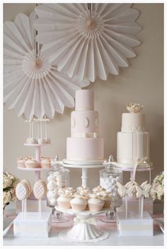 a table topped with cakes and cupcakes next to a wall mounted paper fan