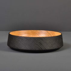 a wooden bowl sitting on top of a gray table next to a black wall and floor