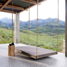 a wooden swing sitting on top of a cement floor next to a lush green hillside