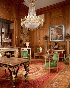 a fancy living room with chandelier, chairs and paintings on the wooden paneled walls