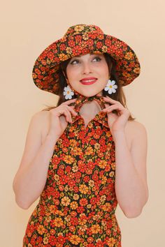 a woman wearing a flowered dress and hat poses for the camera with her hands on her hips