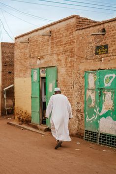 a man walking down the street in front of a building with green doors and graffiti on it