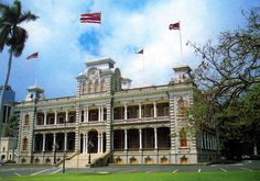 an old building with three flags flying in the wind and palm trees on either side