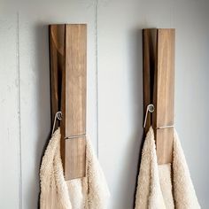 two towels are hanging on the wall next to each other with wooden hooks holding them