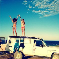 two women in bikinis standing on top of a van