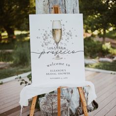 a welcome sign with a glass of champagne on it sitting in front of a tree