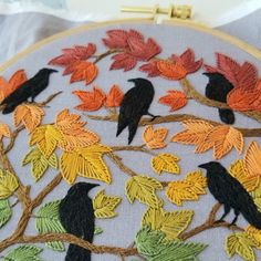 two black birds sitting on a tree branch with autumn leaves in the background and a gold frame