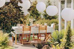 an outdoor dining table with four chairs and white paper lanterns hanging from the ceiling over it