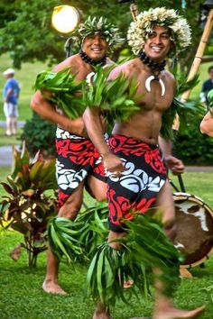 two men in hawaiian costumes are dancing on the grass