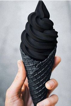 a hand holding an ice cream cone with black icing on it's tip