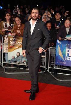 a man in a suit and tie standing on a red carpet at a film festival