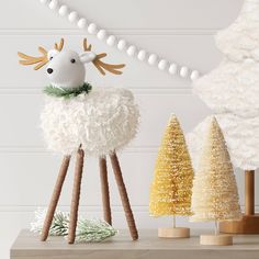 a white sheep standing on top of a wooden stand next to two small christmas trees