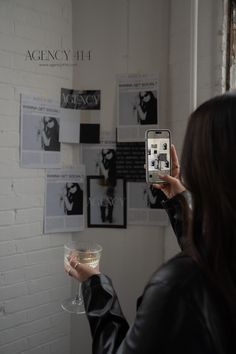 a woman taking a selfie with her cell phone in front of a white brick wall