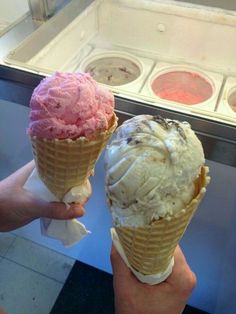 two ice cream cones are being held up in front of an ice cream display case