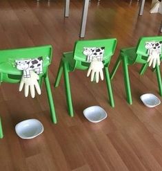 three green chairs with painted hands on them in the middle of a wooden floored room