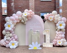 a birthday party with balloons and flowers on the front of a brick building, including a cake stand