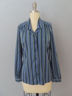 Vintage 70's long sleeve disco blouse. Super soft in medium blue with dark blue, white and green vertical stripes. Cutaway collar with button-up front. Fabric colored buttons. Slim fit style. Long sleeves with button cuffs. Straight hem. Fits a modern day women's size large. Please see measurements below. MEASUREMENTS--Taken with garment laying flat, in inches, doubled: Chest: 42"  Waist: 36"  Shoulder: 16" Sleeves: 23" Length: 24" Label/ Era: Panther| 1970 Fabric: Polyester, fabric covered buttons Condition: Excellent condition. Freshly laundered and no known issues. ★ Shop the entire shop here: https://www.etsy.com/shop/retrosuzysvintage Instagram | retrosuzysvintage Facebook | retrosuzysvintage Pinterest | retrosuzysvintage Blue Vertical Striped Collared Top, Collared Tops With Vertical Stripes For Fall, Blue Long Sleeve Tops With Vertical Stripes, Blue Long Sleeve Blouse With Vertical Stripes, Blue Vertical Stripes Button-up Blouse, Fitted Button-up Tops With Vertical Stripes, Fitted Vertical Stripe Button-up Tops, Blue Fitted Tops With Vertical Stripes, Fitted Blue Tops With Vertical Stripes