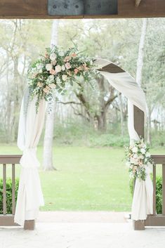 an outdoor wedding ceremony setup with white drapes and flowers on the arch, along with greenery