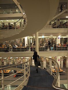 a woman walking down a spiral staircase in a large library filled with bookshelves